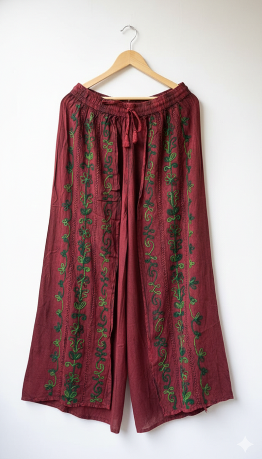 Red pants with green patterns hanging on a wooden hanger against a white background
